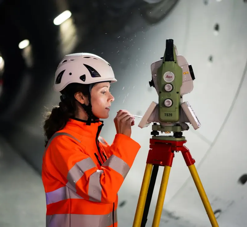 Geodetka w kasku przy tachimetrze Leica TS20 na statywie w tunelu